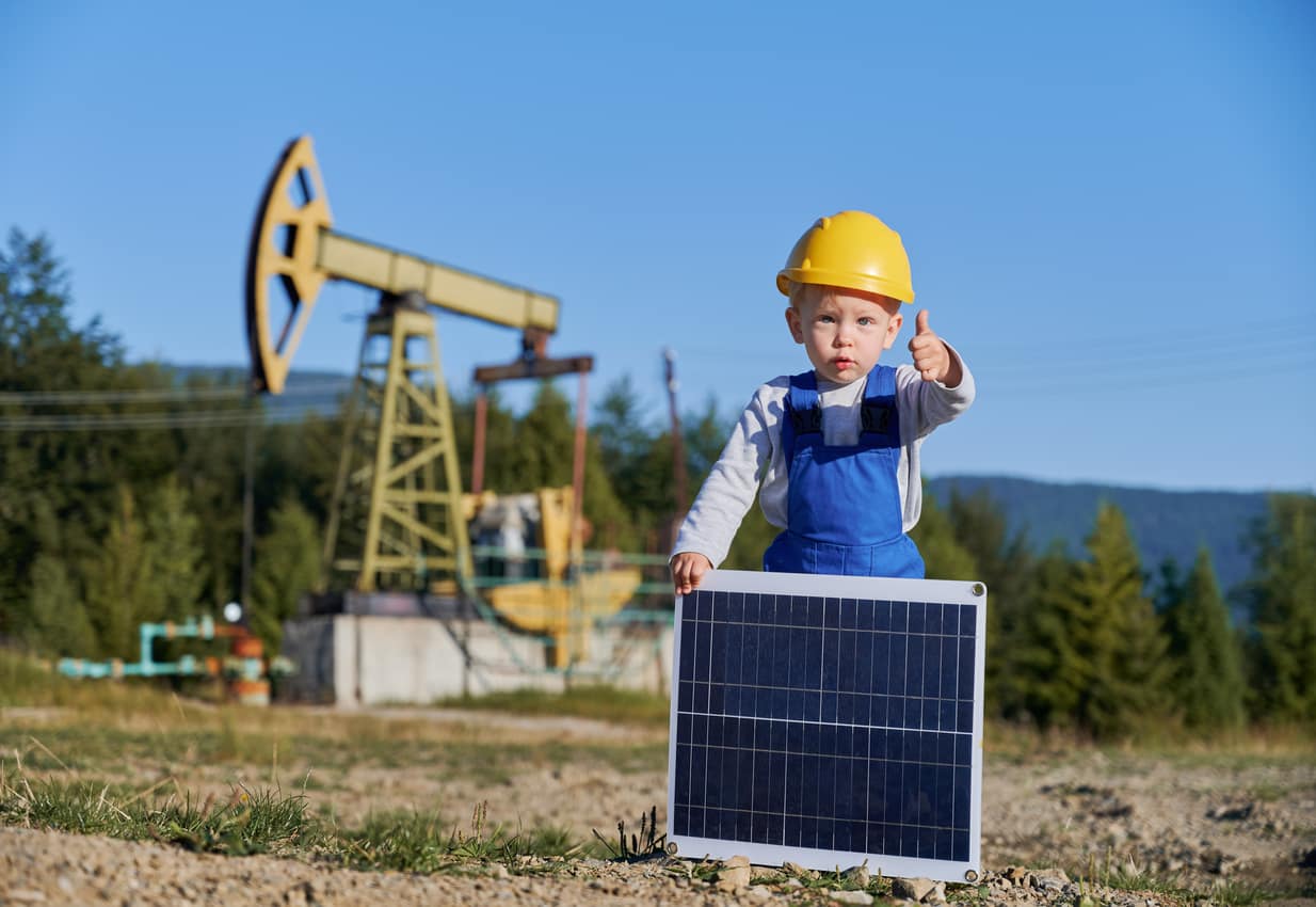 Male child with solar panel showing thumb up against petroleum pump - Evergreen Off-Grid